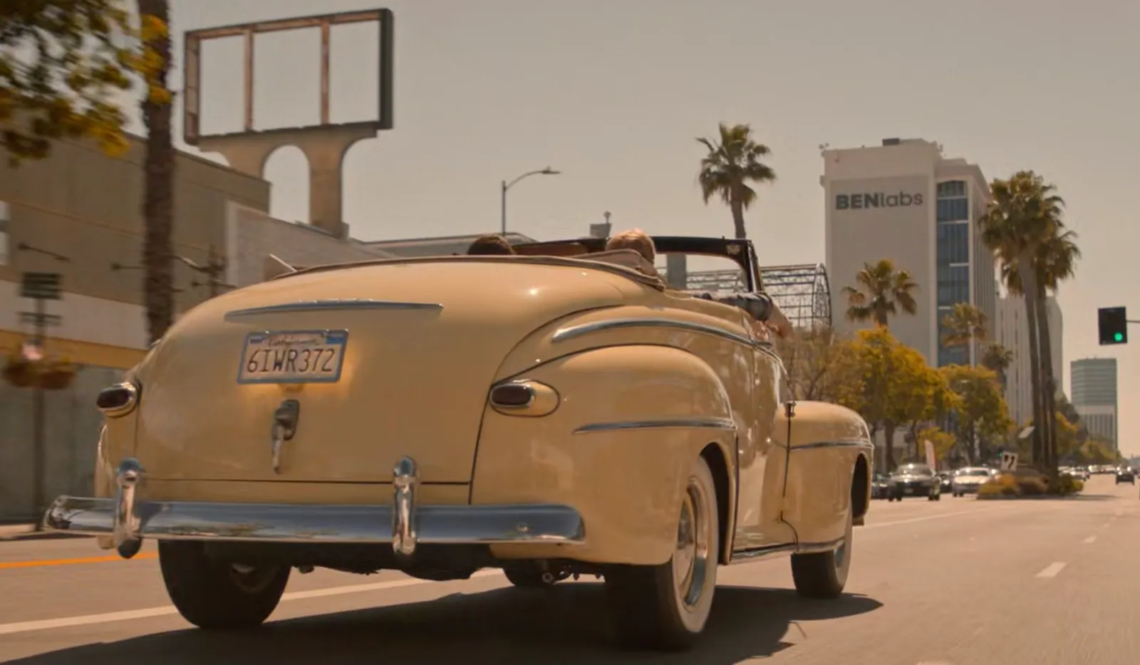 A vintage cream convertible driving away down a wide, palm-lined Los Angeles boulevard. In the background a white office tower carries the BENlabs sign.